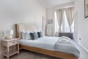 Et soveværelse med seng, sengebord, lampe og et vindue med gardiner.