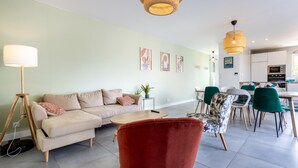 A modern living room with a sofa, red chair, dining table, and kitchen area. - Holiday Home “Maison Concarneau” with Private Terrace, Garden & Wi-Fi (Concarneau)