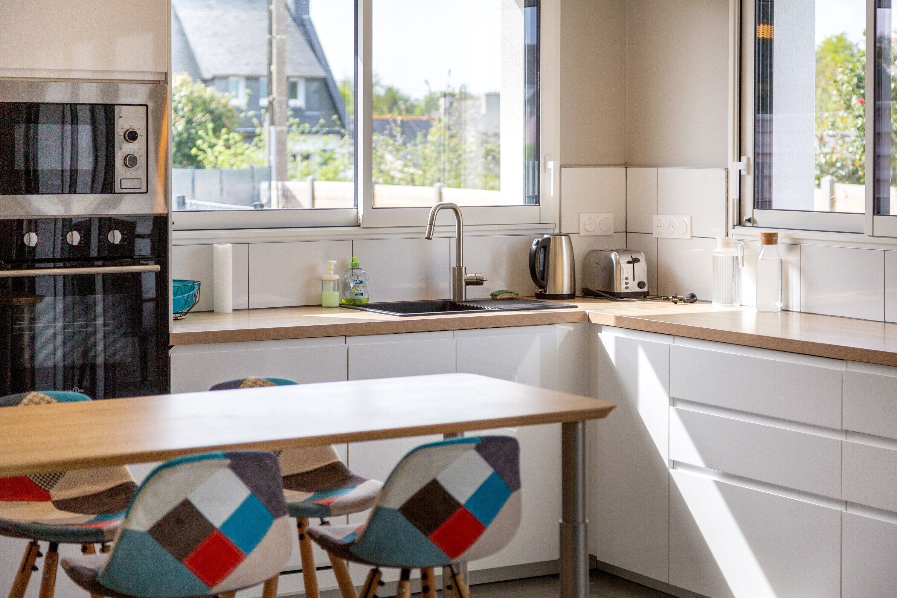 Une cuisine moderne dotée d’une fenêtre, d’un évier, d’une cuisinière et d’un coin repas avec des chaises.