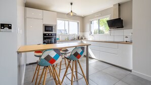 A modern kitchen with white cabinets, a wooden countertop, a built-in microwave, and a large window. - Holiday Home “Maison Concarneau” with Private Terrace, Garden & Wi-Fi (Concarneau)