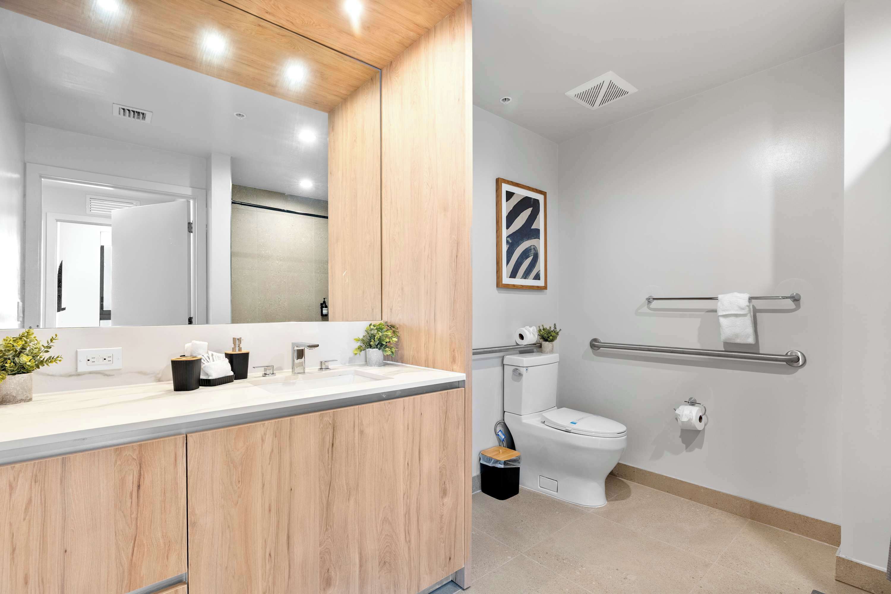 Un baño moderno con tocador de madera, inodoro, barra de apoyo y perchero.