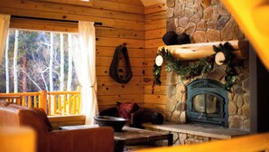 A log cabin interior with a stone fireplace, wooden walls, a wooden bench, and a view of trees outside. - Lakeview Mountain Cabin with Wraparound Deck, Hot Tub & Wood Burning Fireplace. (Twin Lakes)