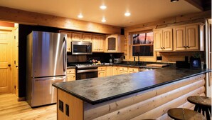 A modern kitchen with wooden cabinets, stainless steel appliances, and a bar area with stools. - Lakeview Mountain Cabin with Wraparound Deck, Hot Tub & Wood Burning Fireplace. (Twin Lakes)