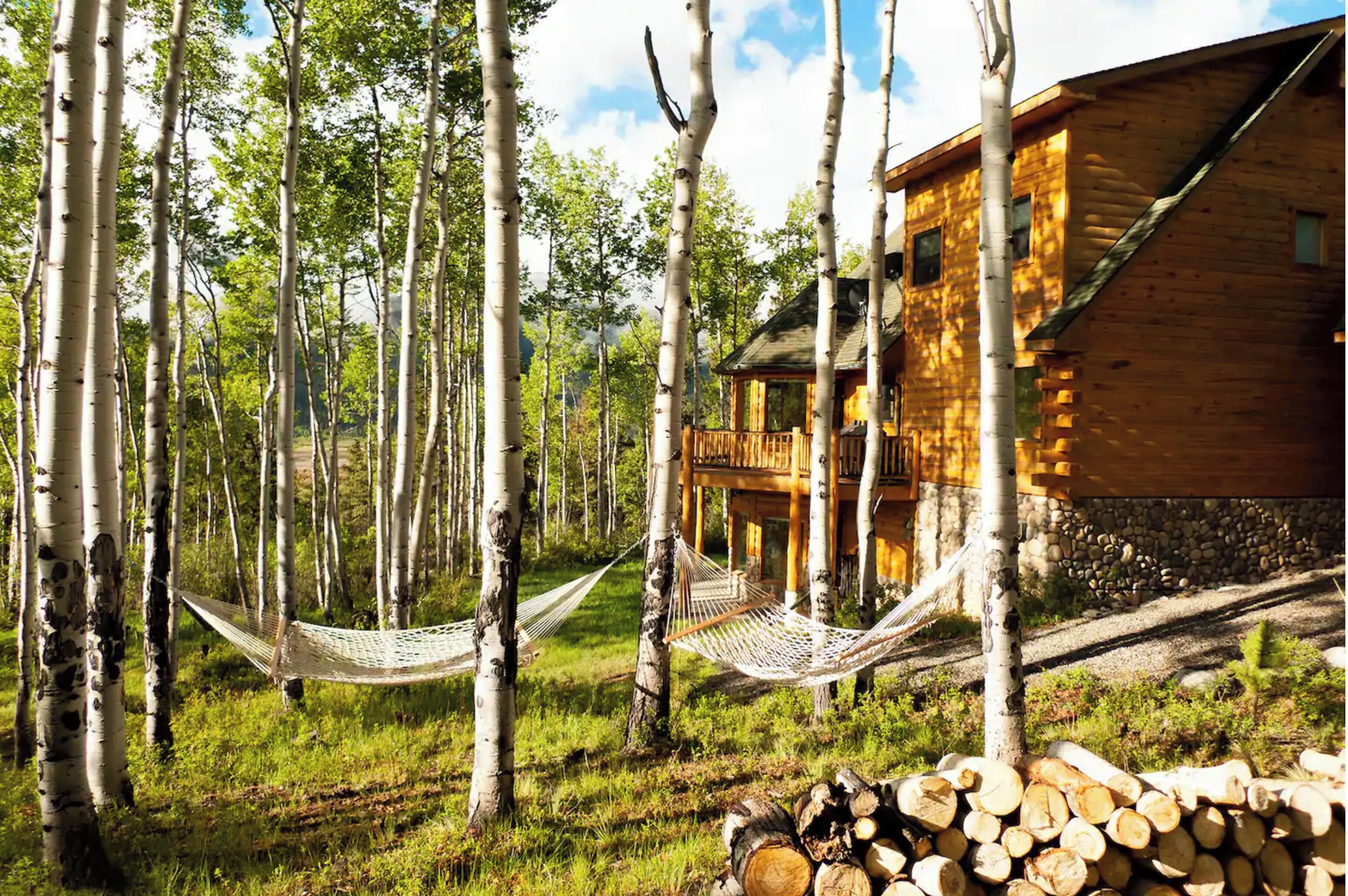 Una cabaña de madera con terraza, rodeada de abedules y una hamaca.