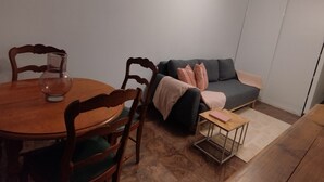 A dining area with a round table and chairs, a sofa with cushions, and a small side table with a book.