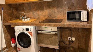 A compact kitchen with a washing machine, a microwave, and wooden cabinets.