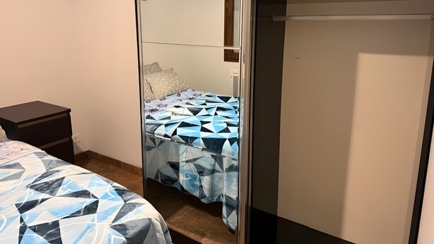 A bedroom with a bed, a nightstand, a wardrobe, and a mirror.