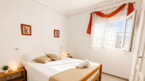 A bedroom with a bed, bedside tables, a window with curtains, and two wall-mounted pictures. - Playa Flamenca With Terrace (Orihuela)