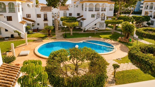 A pool surrounded by manicured gardens and white buildings with terracotta roofs. - Playa Flamenca With Terrace (Orihuela)