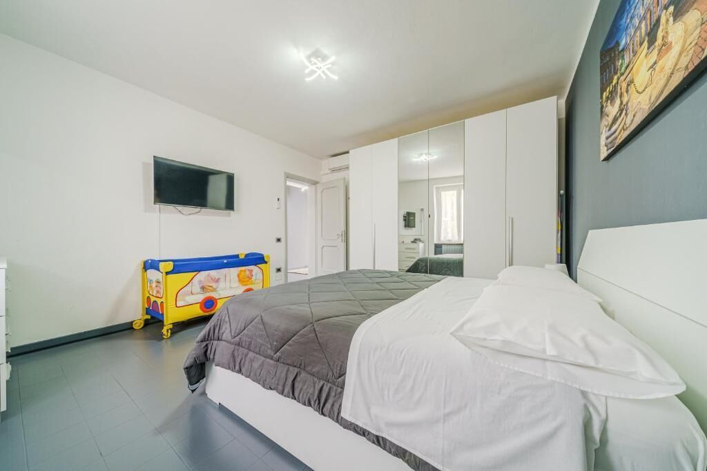 Ein Schlafzimmer mit einem Bett, einem an der Wand befestigten Fernseher, einem Spielwagen für Kinder und einem Bild an der Wand.