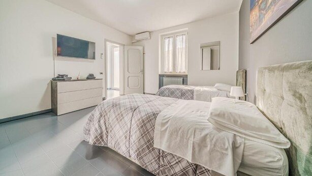 A bedroom with two beds, a dresser, a TV, and a painting on the wall. - Casa Francesco - close to the airport (Azzano San Paolo)
