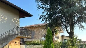 A stone-paved courtyard with a staircase leading to a balcony, surrounded by greenery and a stone building. - Casa Francesco - close to the airport (Azzano San Paolo)