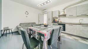 A modern kitchen with grey cabinets, a dining table with a patterned tablecloth, and a grey sofa. - Casa Francesco - close to the airport (Azzano San Paolo)