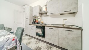 A compact kitchen with a built-in oven, a sink, and a stove. There is a dining table with chairs and a patterned rug. - Casa Francesco - close to the airport (Azzano San Paolo)