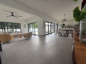 A spacious living area with a sofa, chairs, a coffee table, a dining table with chairs, a kitchen area, and large windows. - modern Caribbean luxury in this stunning 4-bedroom villa in Puerto Plata (Urb El Doral)
