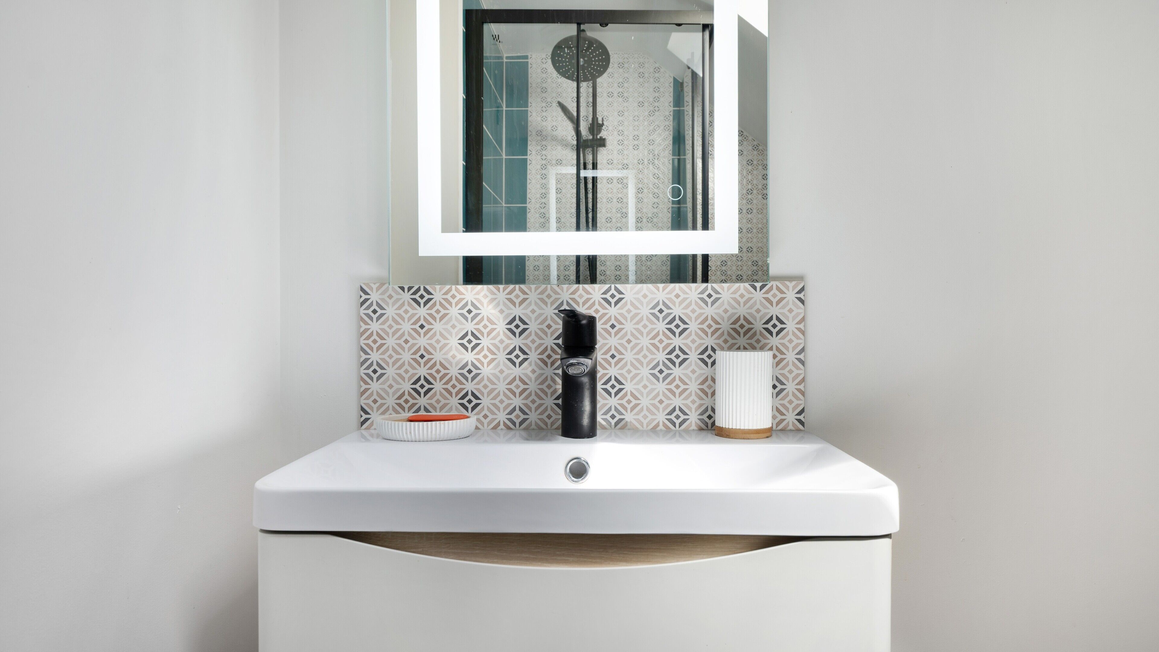 A bathroom with a white sink, a mirror, a shower, and patterned tiles.