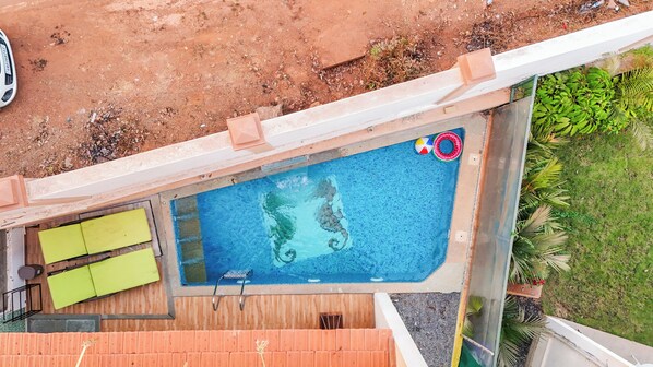 Vista aérea de una piscina con muelle de madera, un bote pequeño y un balón de playa.
