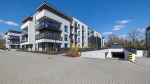 Un immeuble résidentiel moderne à plusieurs étages, doté de balcons, d’un garage et d’une allée pavée.