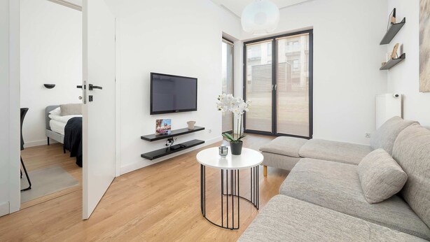 Un salon moderne avec un canapé, une table basse ronde, un téléviseur et une grande fenêtre.