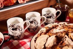 A table with three white mugs with black floral designs, a plate with a round baked good, and a glass of dark liquid. - Mama Shelter Lake Como  (Como)