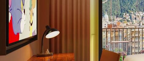 A hotel room with a wooden desk, a laptop, a chessboard, a lamp, a bed, and a view of a cityscape.