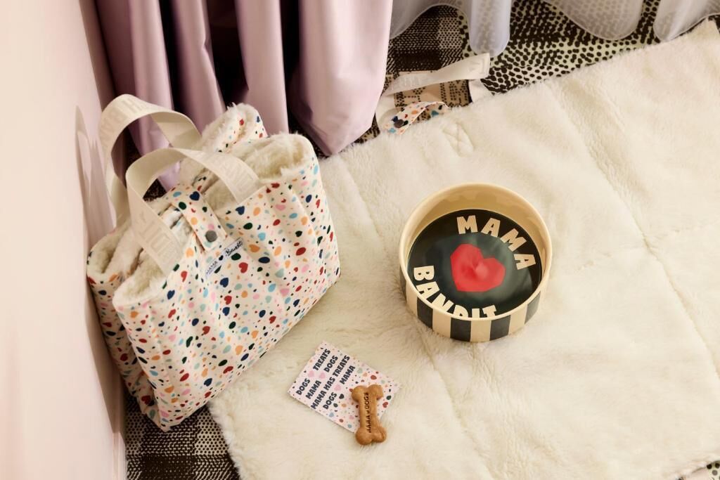 Un tapis blanc et moelleux, un sac à pois, une tasse en bois avec l’inscription « MAMA BUBBLE » et un objet en forme d’os.