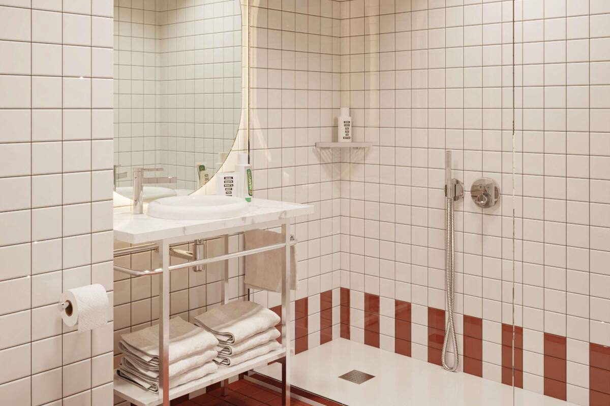 A modern bathroom with a white sink, a mirror, a towel rack, and a shower area.