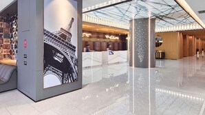 A modern lobby with a large digital screen displaying the Eiffel Tower, a reception area, and a glass ceiling.