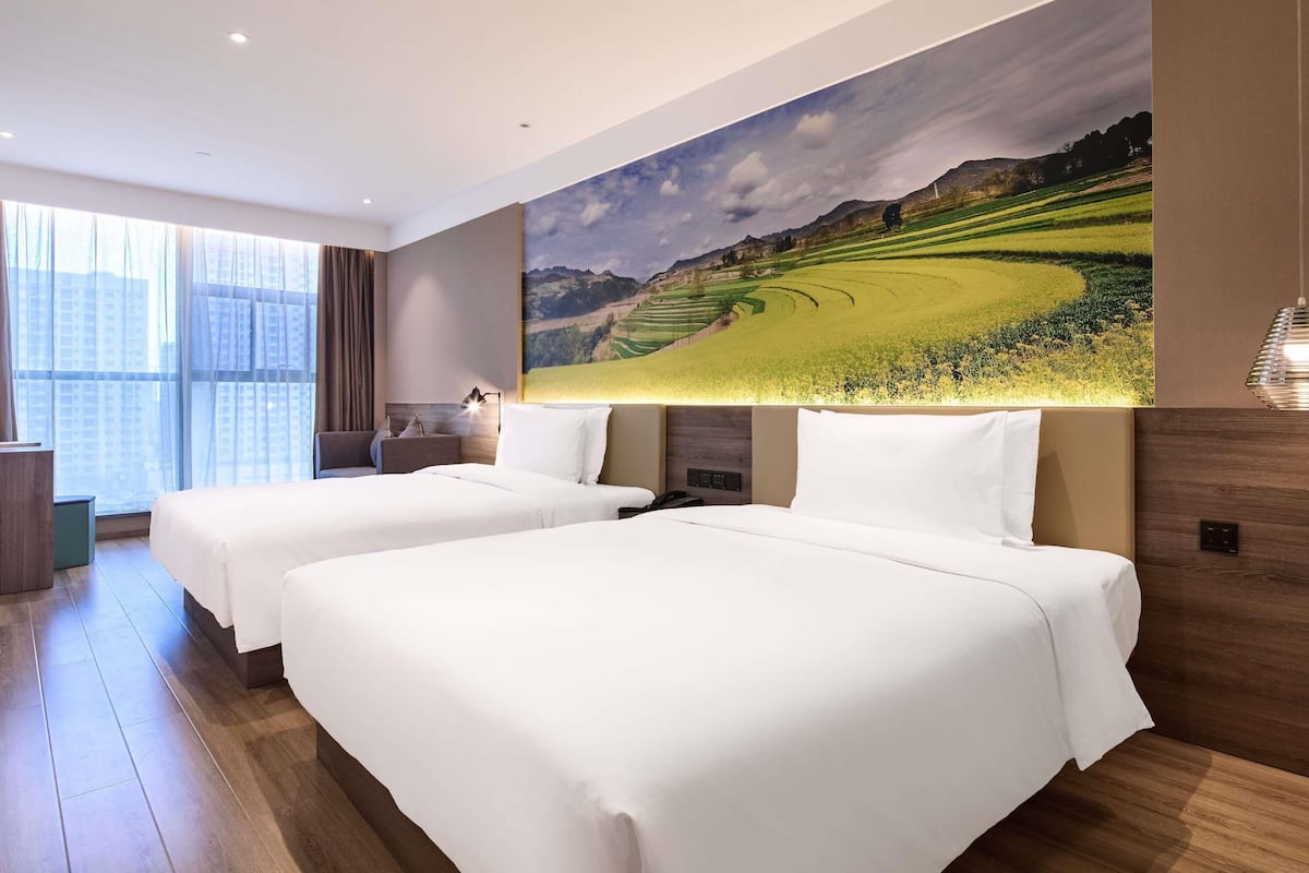 A hotel room with two beds, a large window, and a painting of a landscape.