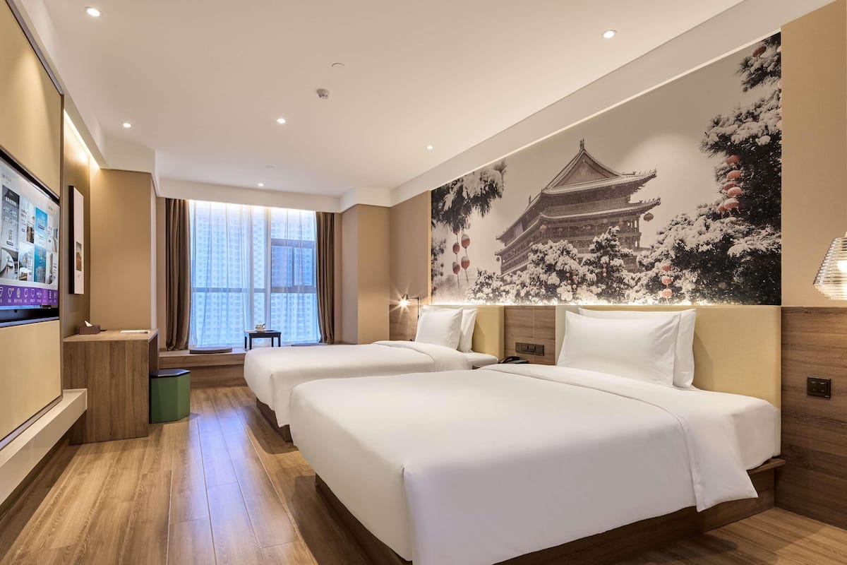 A hotel room with two beds, a large window, a wall-mounted TV, and a traditional-style mural.