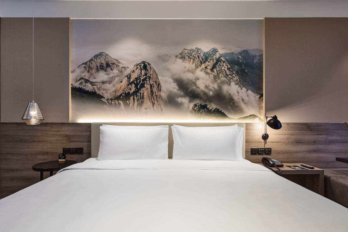 A hotel room with a large bed, a nightstand with a lamp, and a wall-mounted phone.
