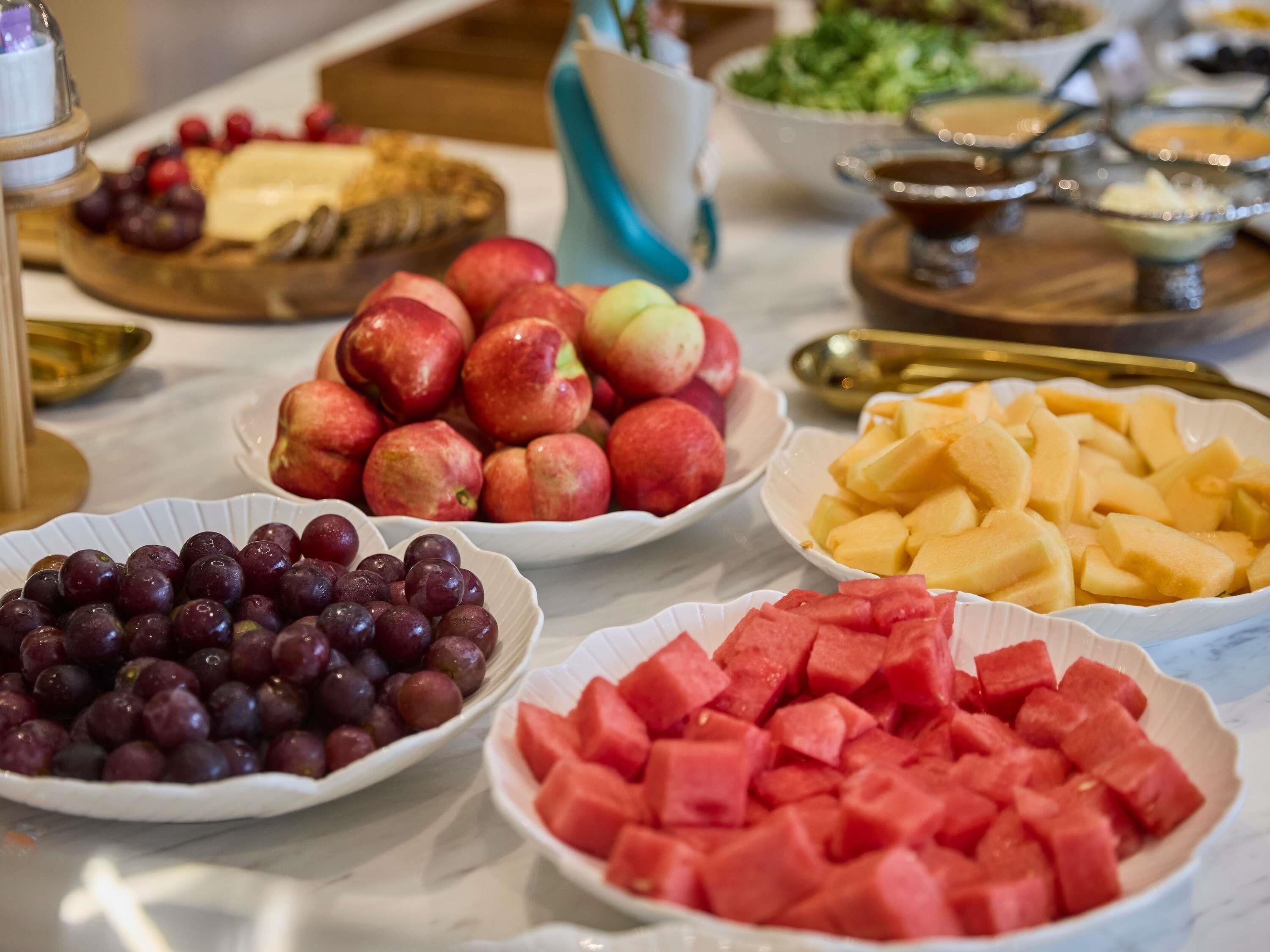 A buffet table with various fruits including grapes, apples, and watermelon.