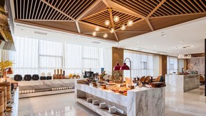 A modern hotel lobby with a marble reception desk, a coffee station, and a seating area.