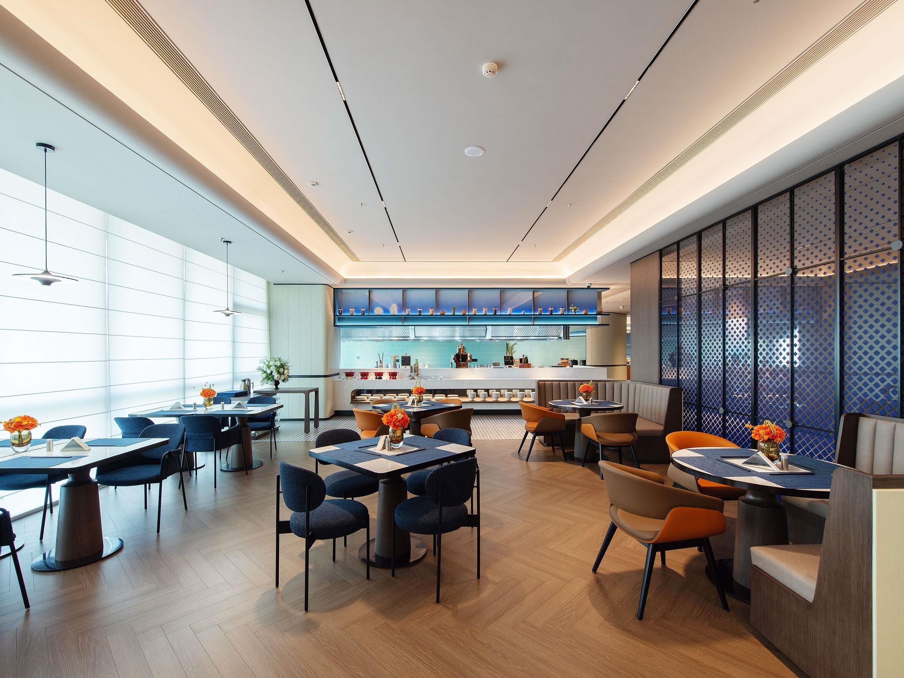 Um restaurante moderno com área de bar, diversas opções de assento e vista para a cozinha.