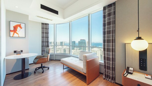 Een moderne hotelkamer met een groot raam, een bank, een kleine tafel en een bureau met een telefoon.