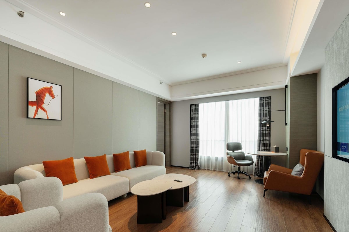 Una sala de estar moderna con un sofá modular, una mesa de centro, una mesa de comedor con sillas y un ventanal con cortinas.