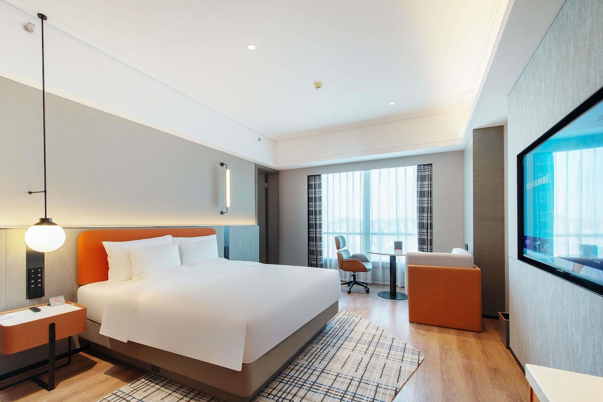 Habitación de hotel moderna con una cama grande, un escritorio, una silla, un televisor y vistas a la ciudad.