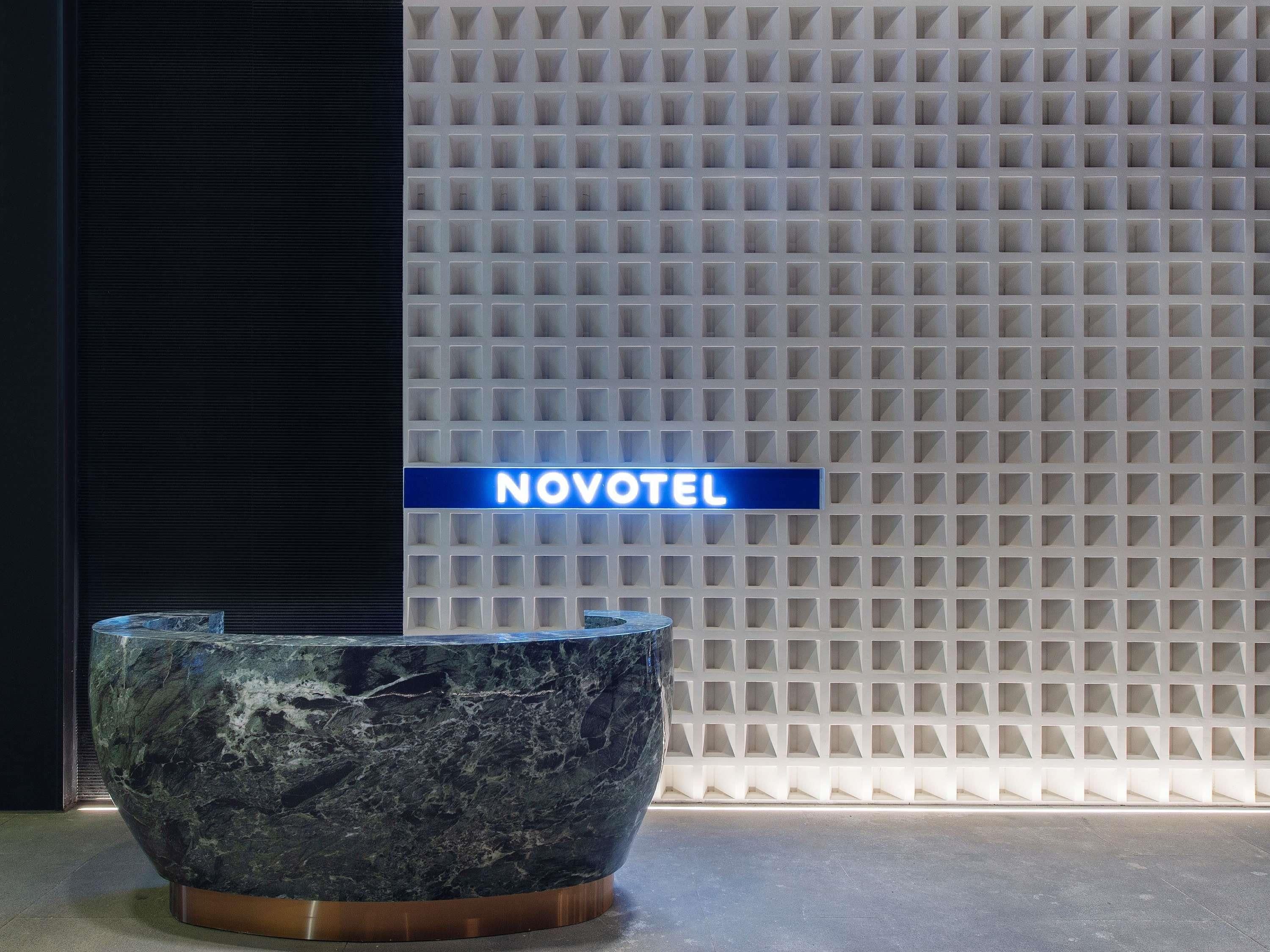 Un mostrador de recepción de mármol con un letrero que dice 'NOVOTEL' frente a una pared con textura.