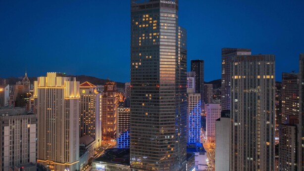 Un hotel moderno de gran altura con fachada de vidrio, rodeado de otros edificios altos en un paisaje urbano.