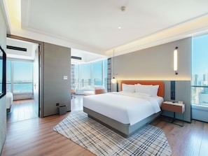 A modern hotel room with a large bed, a desk, a chair, a view of the city, and a large window.