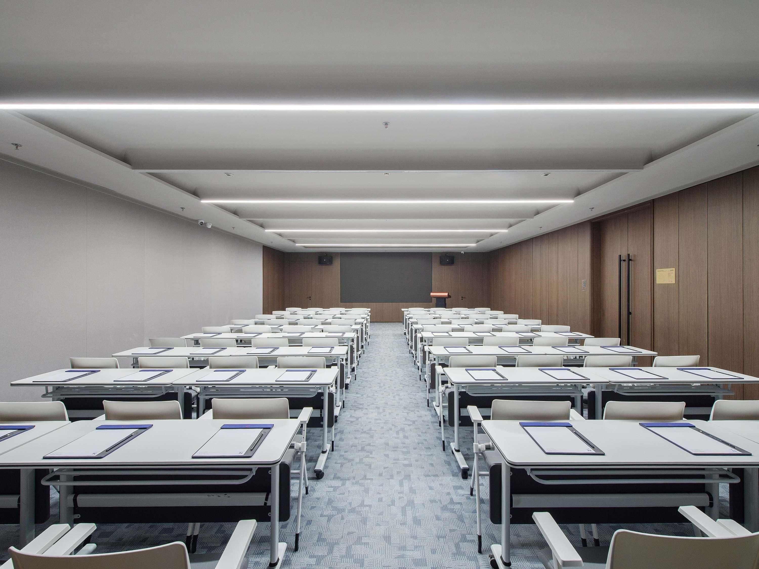 A conference room with rows of tables and chairs, a podium, and a carpeted floor.
