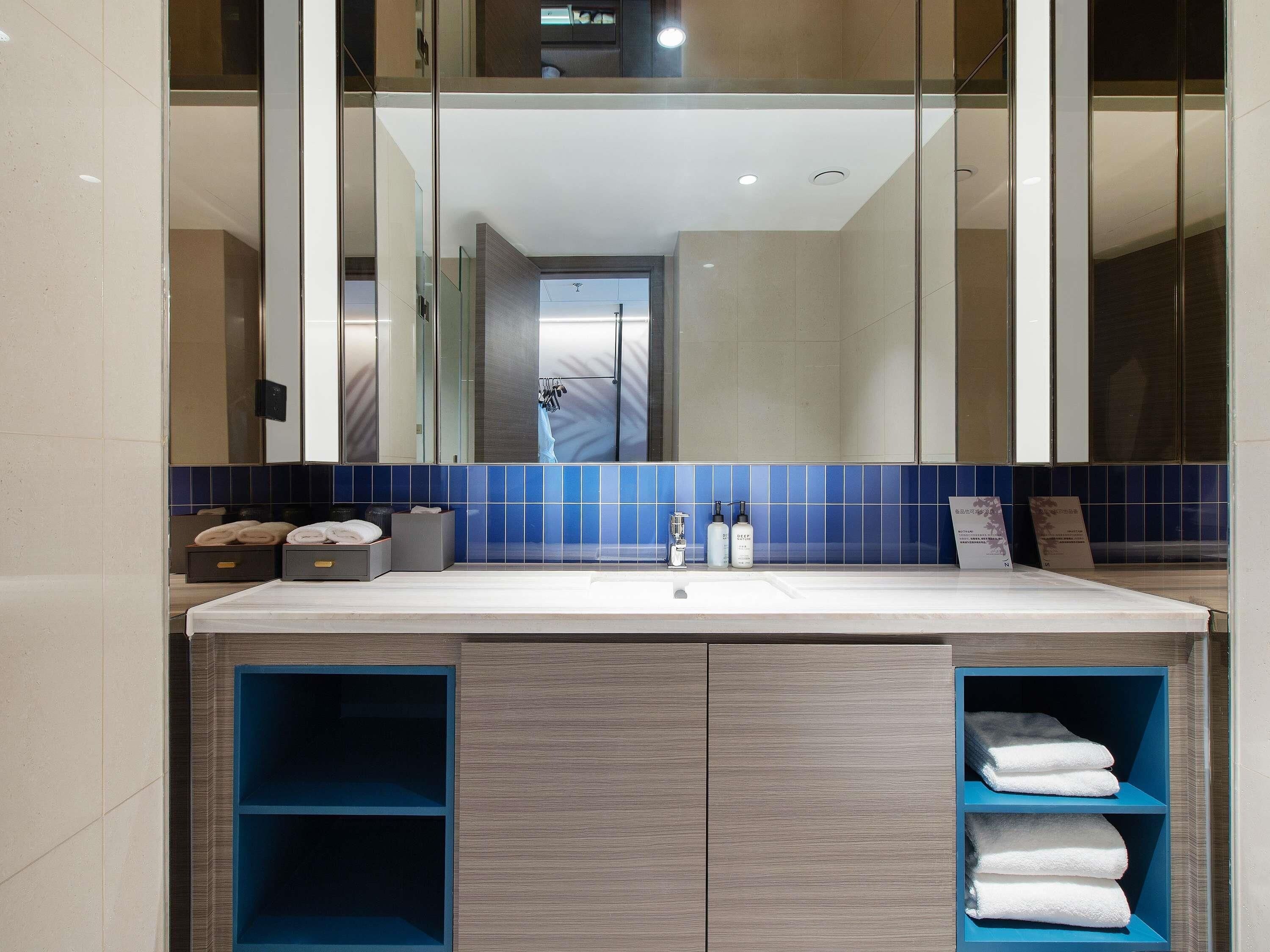 A modern bathroom with a large mirror, a sink, and built-in shelves for towels.