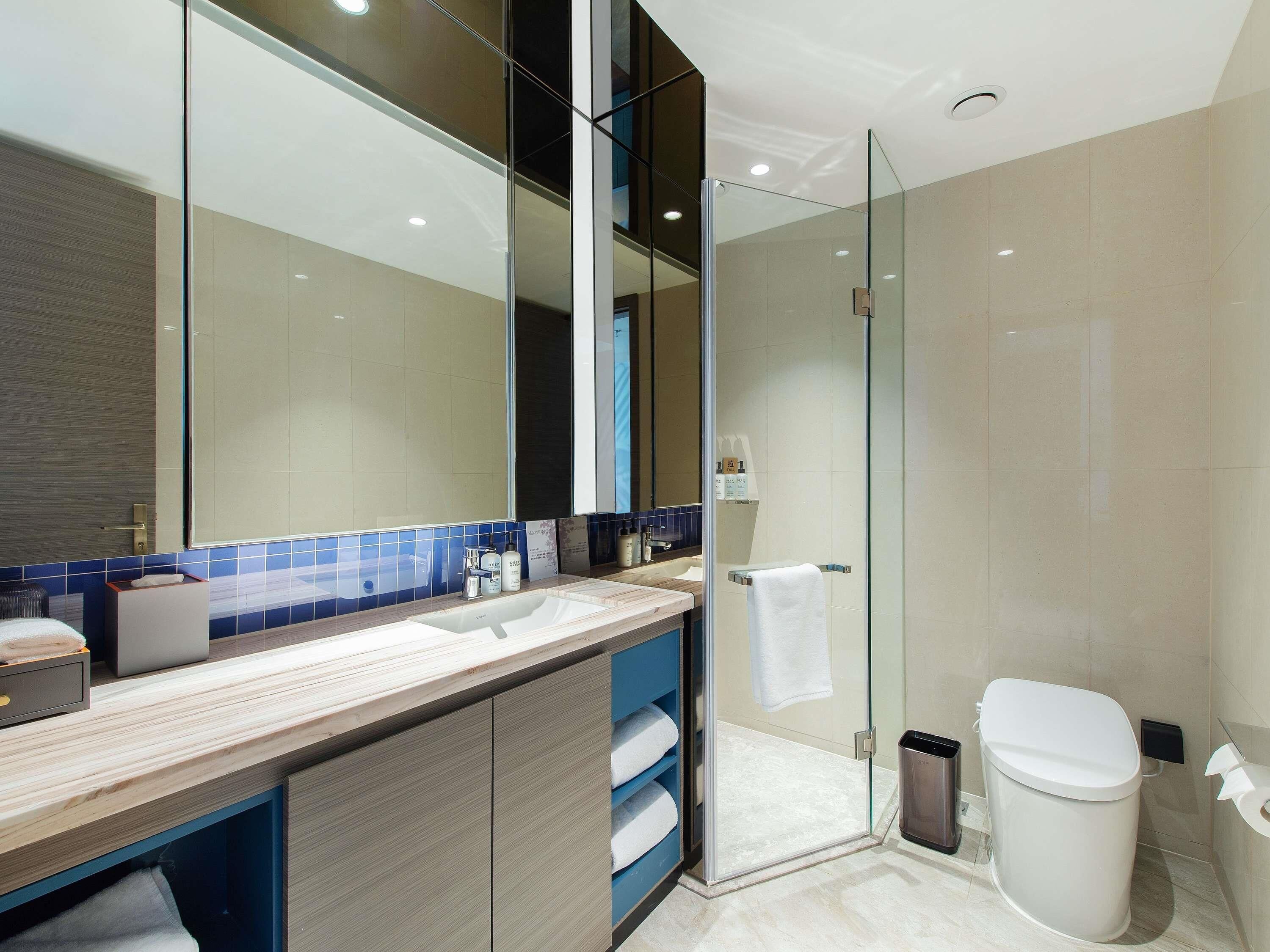 A modern bathroom with a glass shower enclosure, a large mirror, and a wooden vanity.