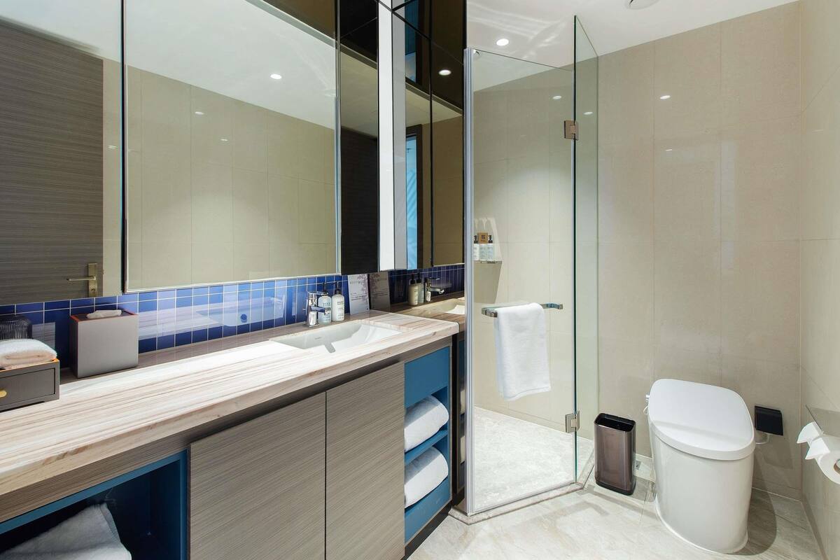 Un baño moderno con cabina de ducha de vidrio, un espejo grande y un mueble de tocador de madera.