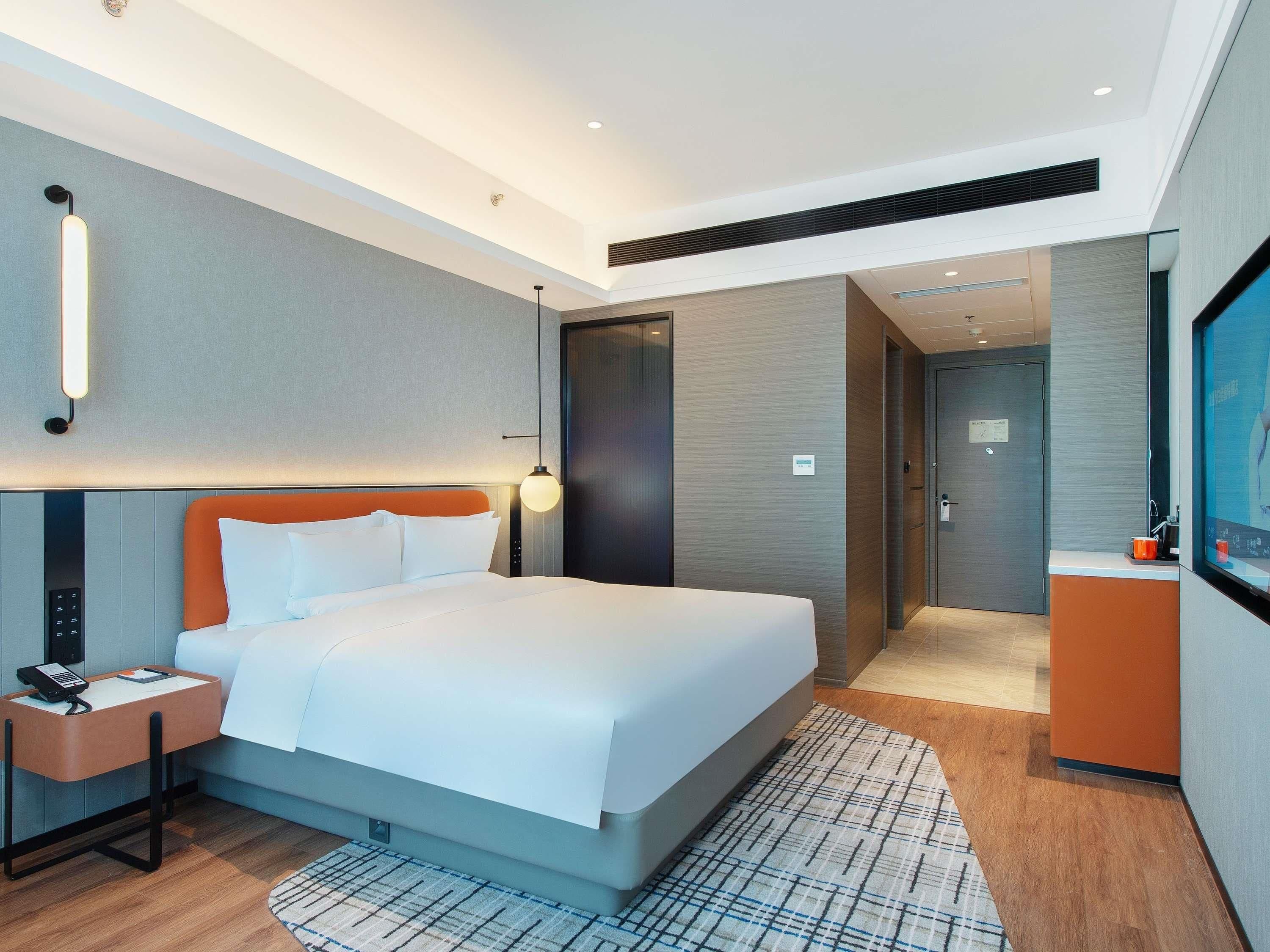 Een moderne hotelkamer met een groot bed, een bureau met telefoon, een wandlamp en een deur naar de badkamer.