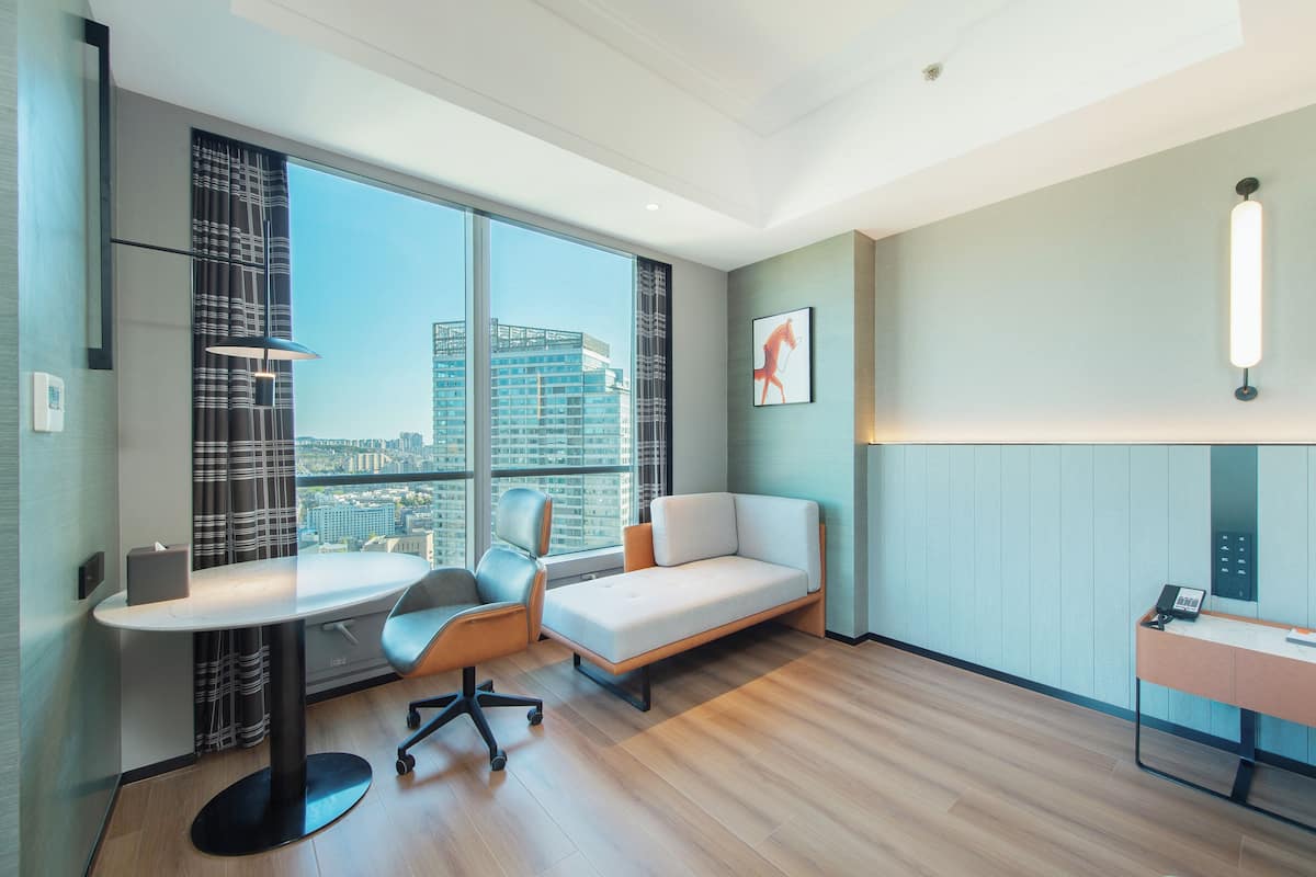 Una habitación de hotel moderna con un ventanal grande, un escritorio, un sofá y un teléfono en la pared.