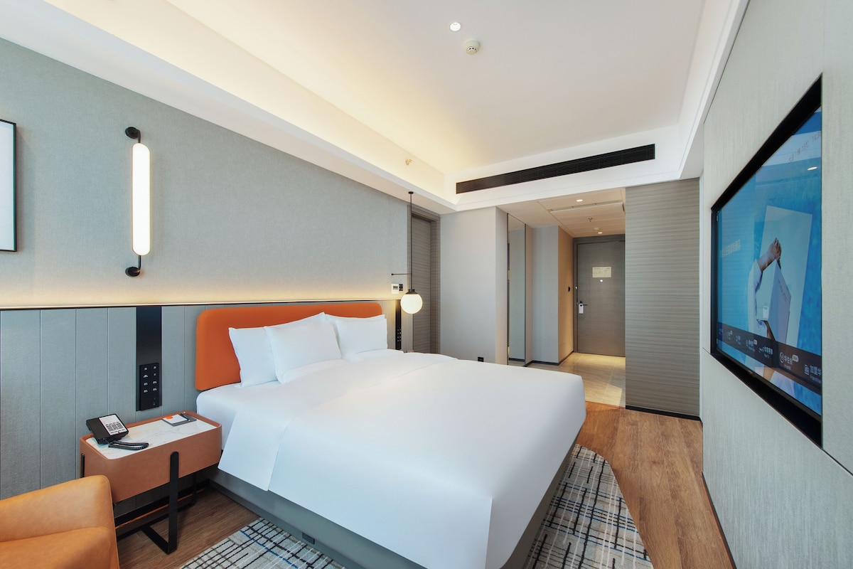 Ein Hotelzimmer mit einem Bett, einem Schreibtisch mit Telefon, einem Fernseher und einem Spiegel.