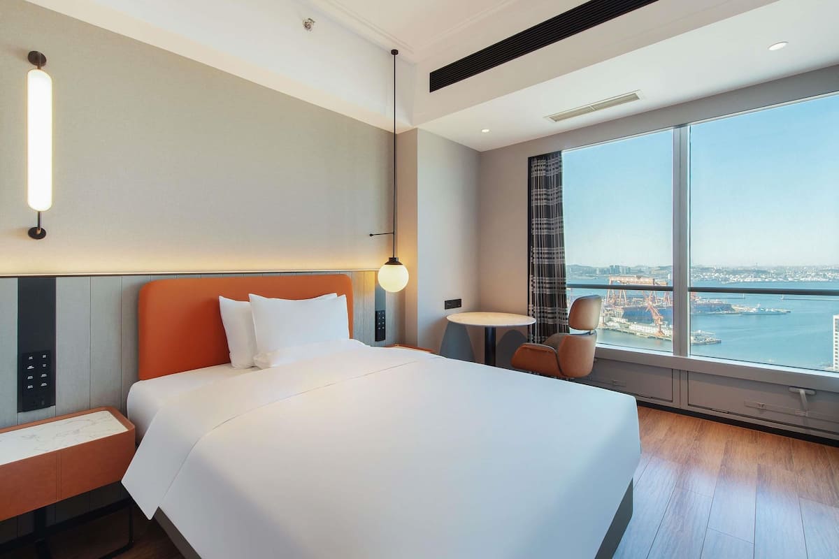Una camera d'albergo con un letto, una scrivania, una sedia, un tavolino e un'ampia finestra con vista sulla città.