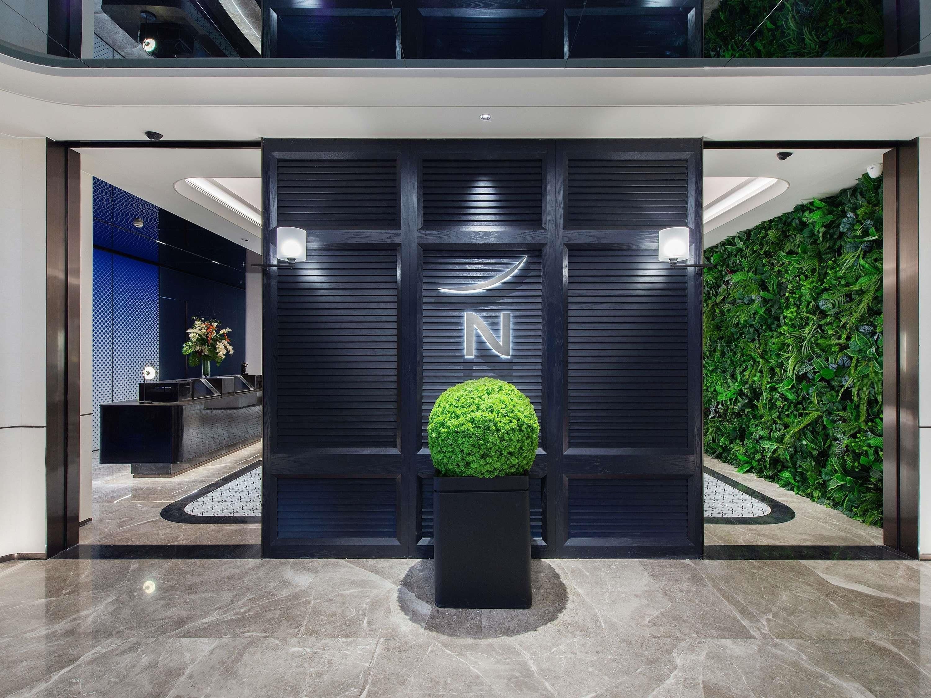 Una zona de recepción moderna con un logotipo, una planta en maceta y una pared verde.