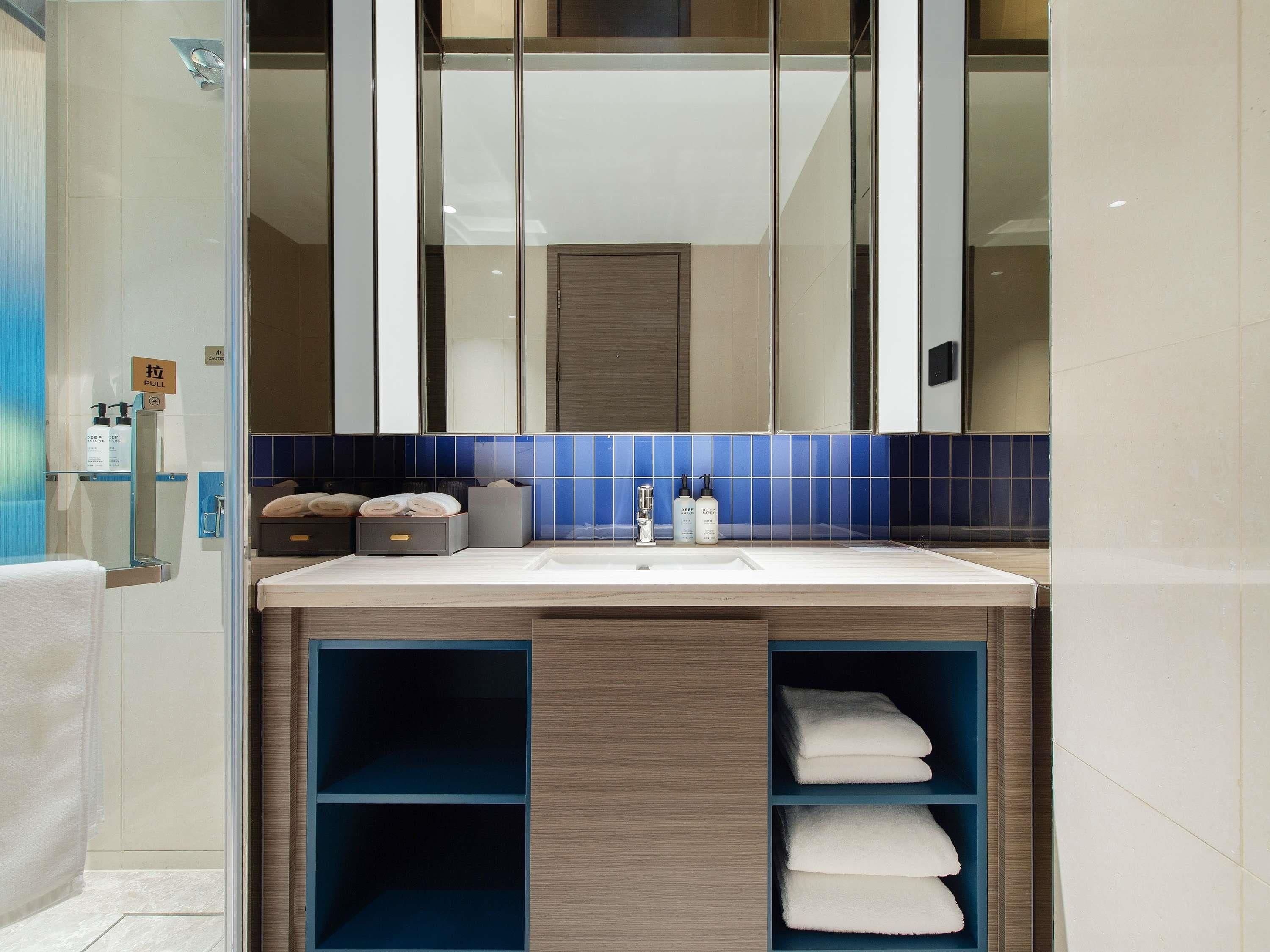 Une salle de bain moderne avec un grand miroir, un lavabo avec des articles de toilette et un porte-serviettes.
